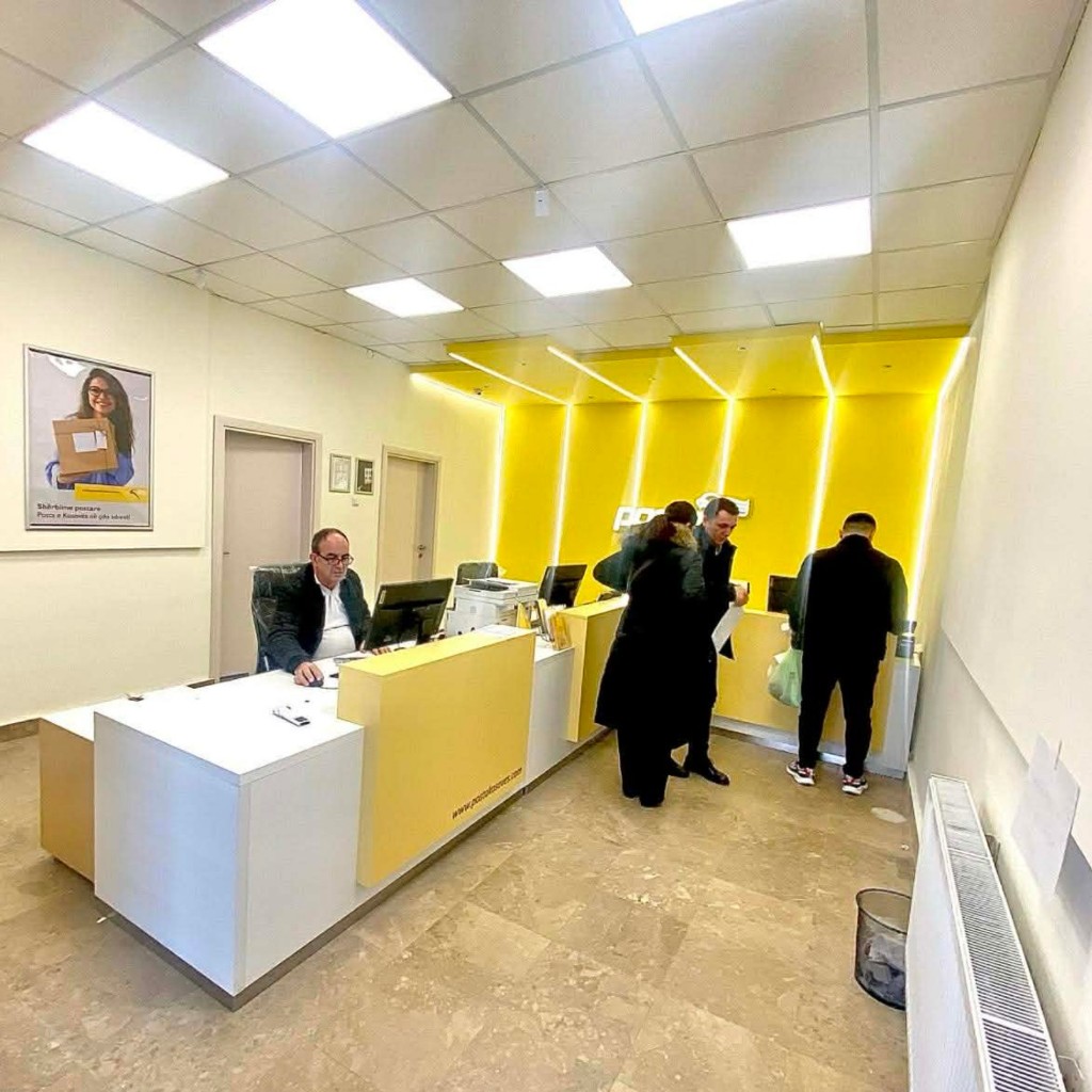 Banak i bardhë dhe i verdhë me punonjës dhe qytetarë në zyrën postare.